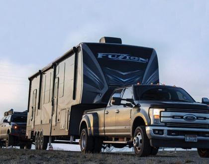 A picture of a Ford pickup truck towing a Fuzion fifth wheel. An SUV follows.