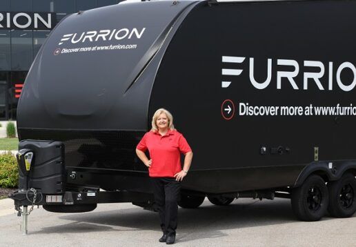 A photo of TracTracy Anglemeyer, Vice President of Sale, Specialty Vehicles. Angelmeyer is standing in front of a travel trailer that says, "Furrion. Discover more at www.furrion.com" on the side.