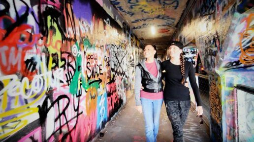 Eli Logue and Anna Wilson walk beside a graffiti-painted wall