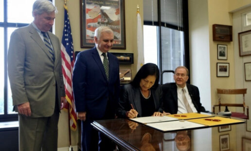 A picture of Interior Secretary Deb Haaland signing at a desk with congressional members around her.