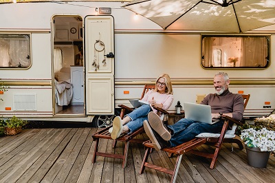 A picture of an elderly couple on loungers outside their RV, using the internet while on a laptop computer