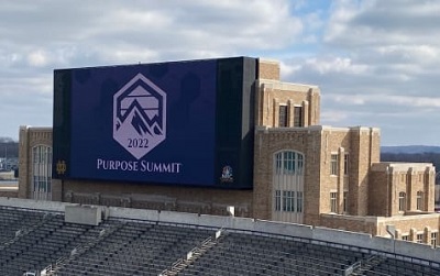 A picture of the Purpose Summit logo displayed on the Notre Dame scoreboard. The event is being co-hosted by Lippert.