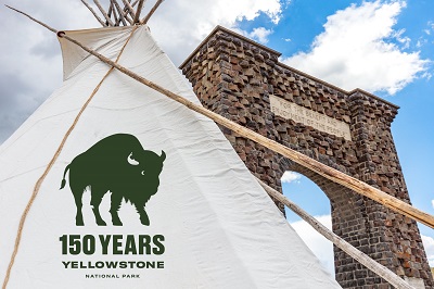 A picture of the Yellowstone 150th anniversary logo on a white flag by an arched park entrance