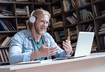 A picture of a man with headphones on in front of a laptop computer talking