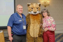 A picture of Brown & Brown Dealer Services President RV F&I Shawn Moran (L) with the Brown & Brown cheetah and Brown & Brown Production Analyst Janet Scavo (R) at the 2024 Brown & Brown F&I School.