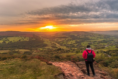 A picture of a hiker on a trail hiking into the sunset over the crest of a hill