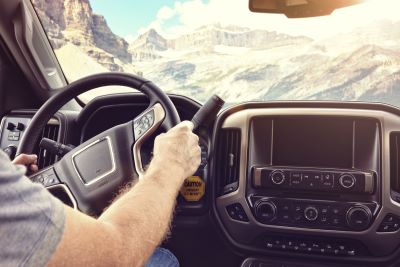 A picture of a male driver in the cockpit of an RV with hands on the steering wheel and a view of mountains through the windshield