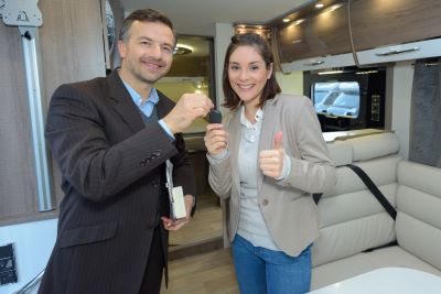 A picture of a young woman being handed keys to an RV by a man in a suit