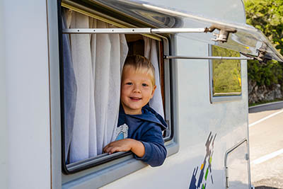 A picture of a little boy in an open camper window looking outside