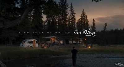 A picture of a man walking back to a campsite, drenched from being in the lake he's walking through with the words "Find Your Wildhood" across the screen.