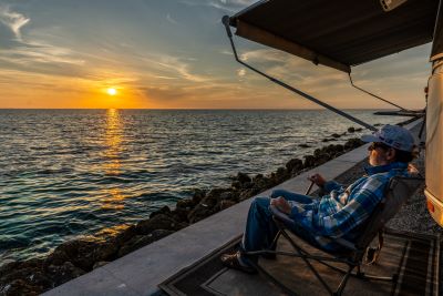 A picture of a man looking out over the water from under an RV awning