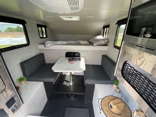 A picture of the Soaring Eagle Adlar 6.5 XL Truck Camper Interior showing a table, cabover bed and seating with a straw hat on it.