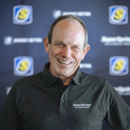 A picture of SuperSprings International Chairman and CEO Gerry Lamberti in front of a wall covered with the company's name and logo.