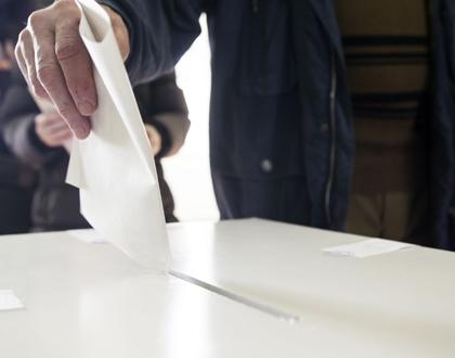 A picture of a hand dropping a ballot into a box.