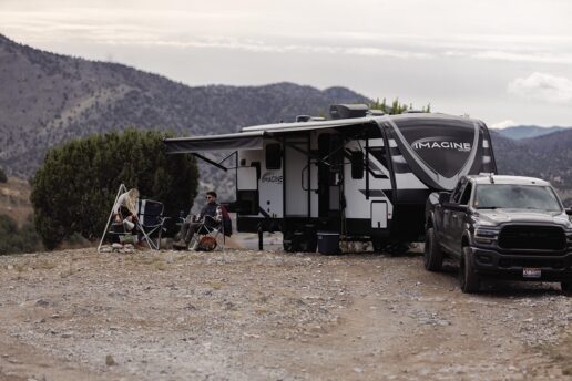 A picture of the Grand Design RV Imagine travel trailer 2024 exterior, with a couple sitting outside the RV.